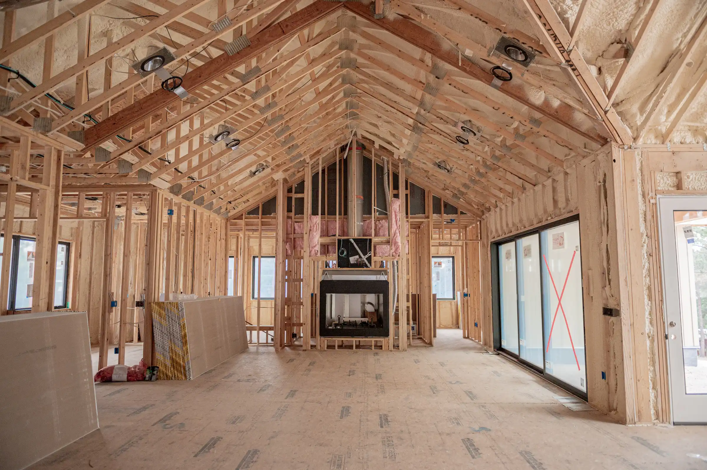 Framed interior of a custom home under construction showing open floor plan, exposed wood beams, insulation, and large window openings.